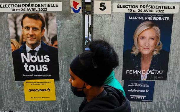 Pedestre passa por cartazes de Emmanuel Macron e Marine Le Pen em 4 de abril de 2022