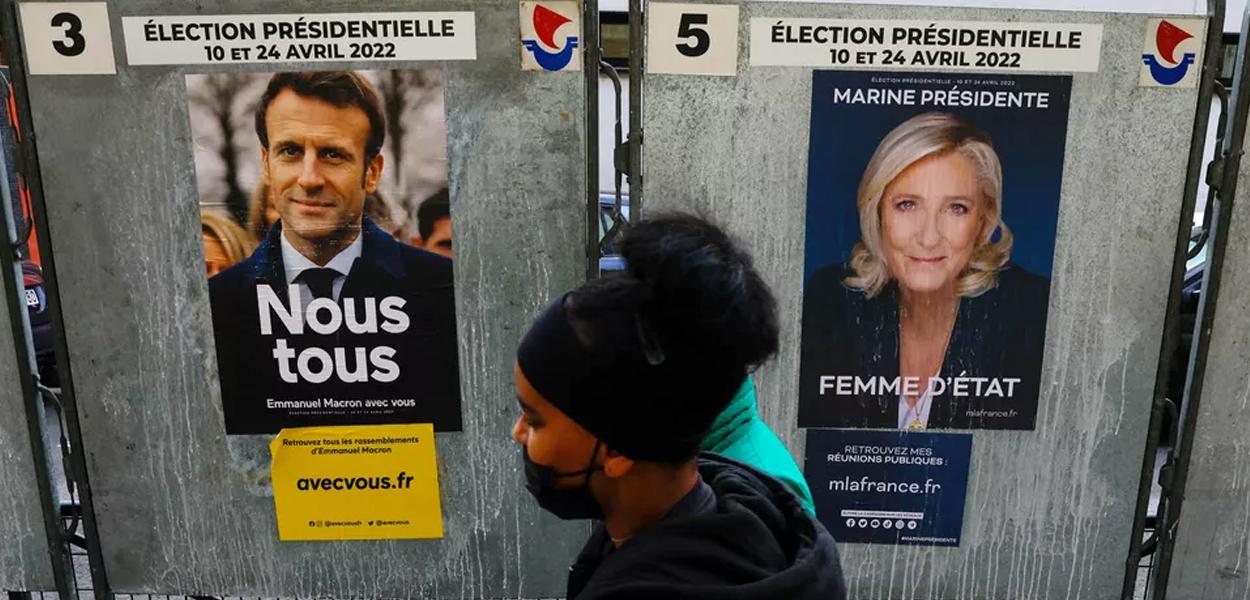 Pedestre passa por cartazes de Emmanuel Macron e Marine Le Pen em 4 de abril de 2022