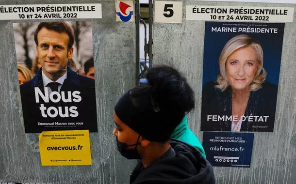 Pedestre passa por cartazes de Emmanuel Macron e Marine Le Pen em 4 de abril de 2022