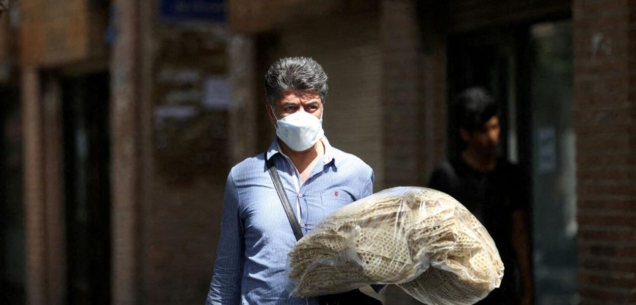 Um homem iraniano segura pilhas de pão enquanto caminha por uma rua em Teerã, Irã, 1º de maio de 2022
