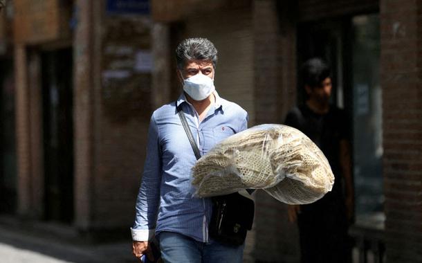 Um homem iraniano segura pilhas de pão enquanto caminha por uma rua em Teerã, Irã, 1º de maio de 2022