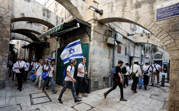Homens judeus carregam bandeiras nacionais israelenses enquanto caminham em um beco, dentro da Cidade Velha de Jerusalém em 29 de maio de 2022