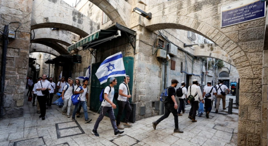 Homens judeus carregam bandeiras nacionais israelenses enquanto caminham em um beco, dentro da Cidade Velha de Jerusalém em 29 de maio de 2022