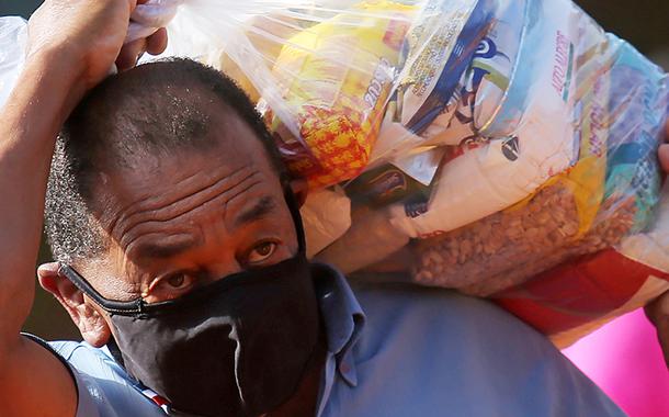 Homem carrega cesta básica destribuída para moradores de favela em São Paulo