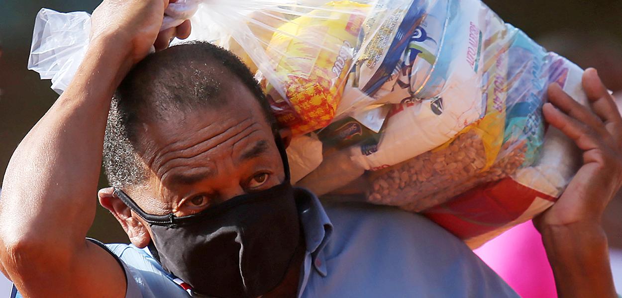 Homem carrega cesta básica destribuída para moradores de favela em São Paulo