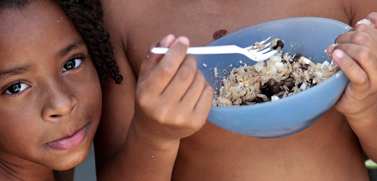 Thawanny Silva de Souza, de 6 anos, (E) e Rafael Silva de Souza, de 9 anos, (D), comem prato com arroz, feijão e ovo na Favela do Arci-Íris, em Recife