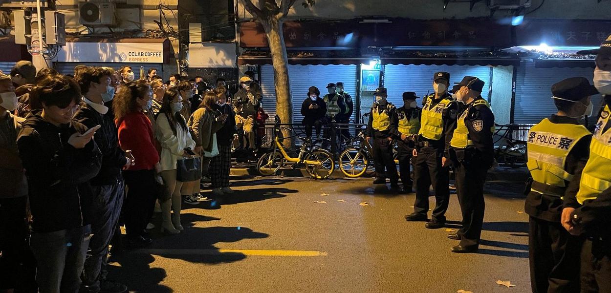 Pessoas ficam em frente a uma fila de policiais durante uma manifestação contra as restrições do COVID-19