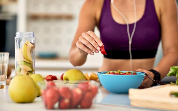 Close-up of athletic woman adding strawberries while making fruit salad in the kitchen.