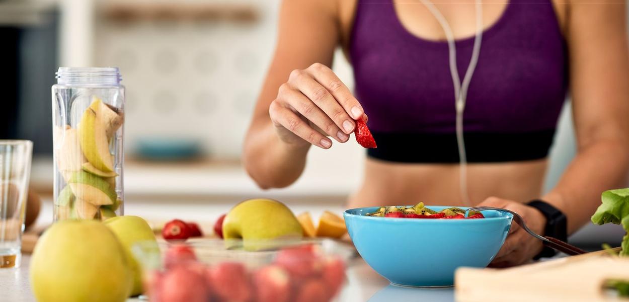 Close-up of athletic woman adding strawberries while making fruit salad in the kitchen.