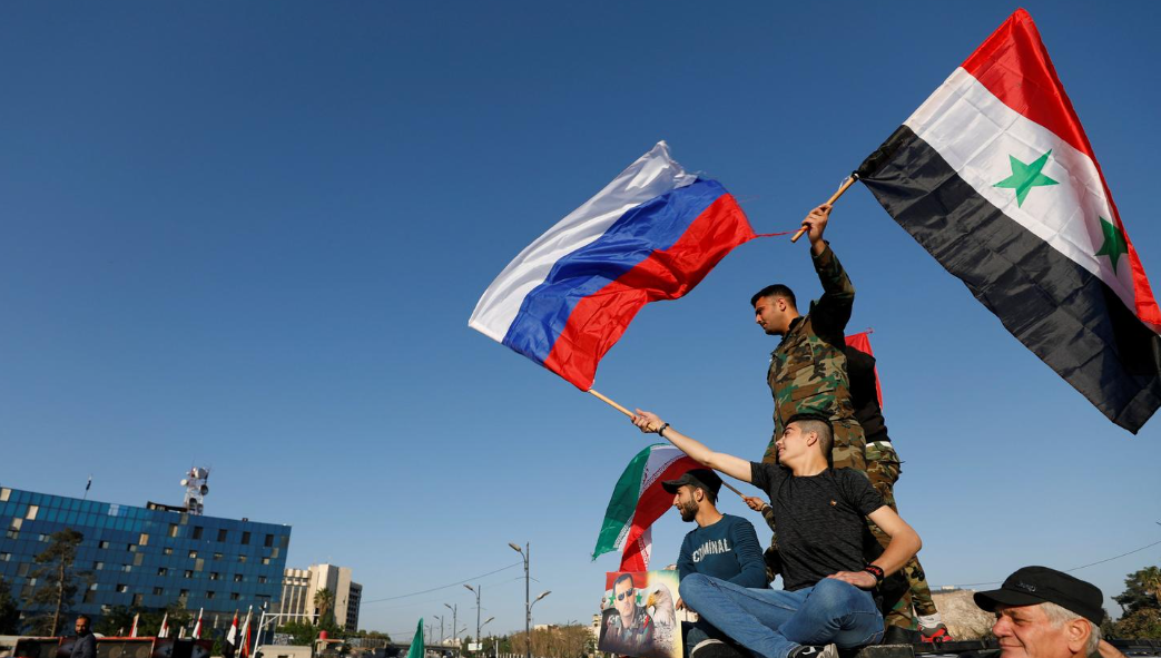 Sírios agitam bandeiras russas e sírias durante protesto contra ataques aéreos liderados pelos EUA em Damasco, Síria, 14 de abril de 2018