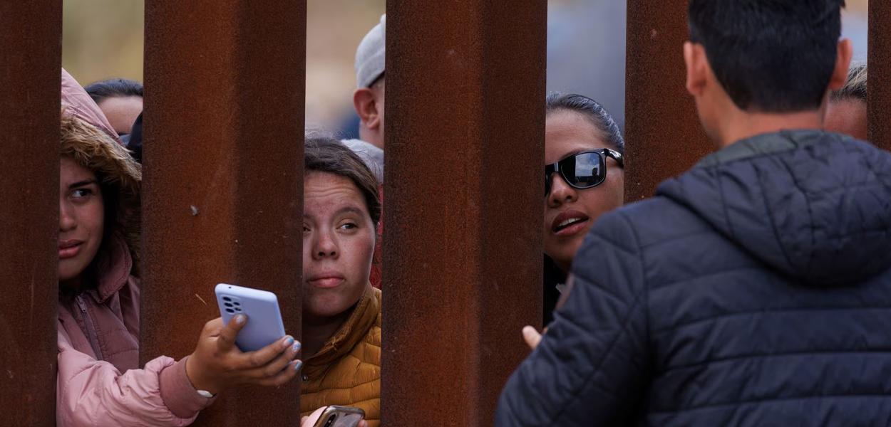 Um menino migrante espera por comida na cerca da fronteira enquanto os migrantes se reúnem entre as cercas primária e secundária da fronteira, perto de San Diego, Califórnia, 10 de maio (Foto: REUTERS/Mike Blake) Um menino migrante espera por comida na cerca da fronteira enquanto os migrantes se reúnem entre as cercas primária e secundária da fronteira, perto de San Diego, Califórnia, 10 de maio