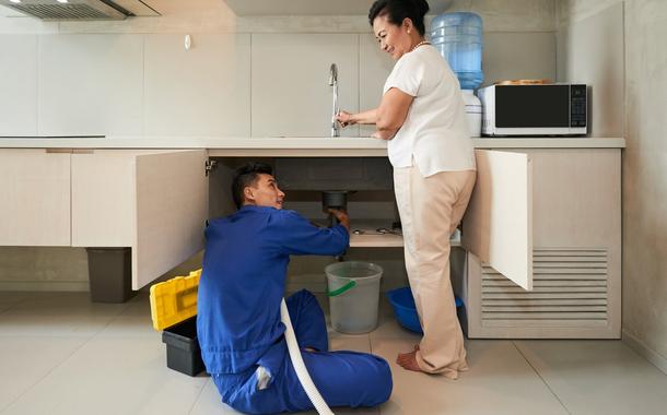 Plumber helping senior woman to change pipe in kitchen