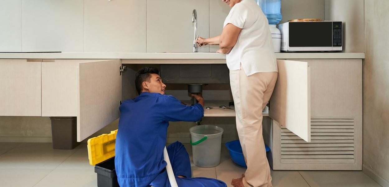 Plumber helping senior woman to change pipe in kitchen